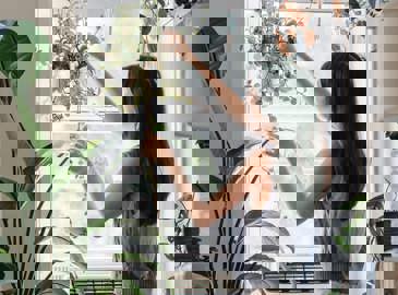 Woman hanging plants in her sunny window 