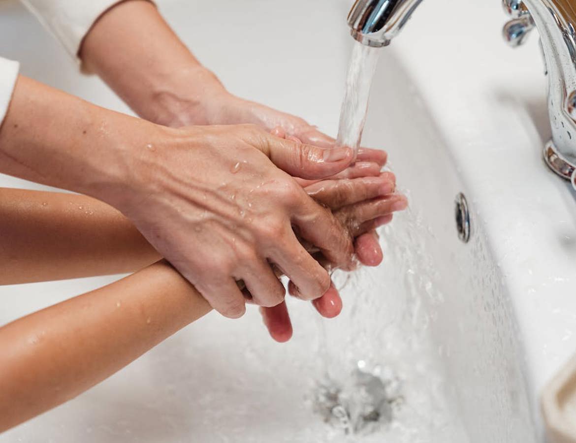 A woman helping a small child to wash their hands in a white sink