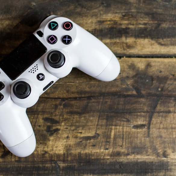 A white Playstation game controller on a wooden table top