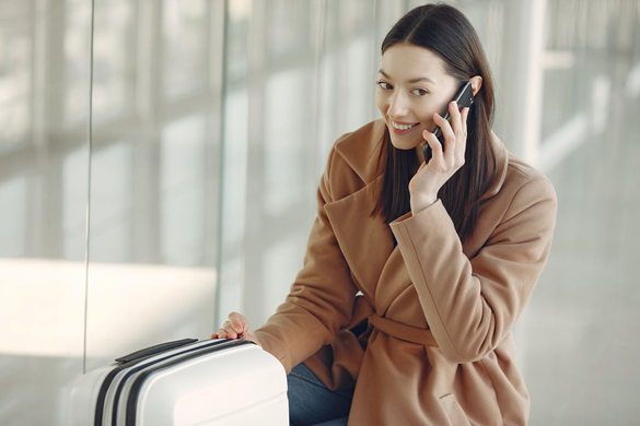 Dark haired woman in a tan coloured coat, talking on the phone 