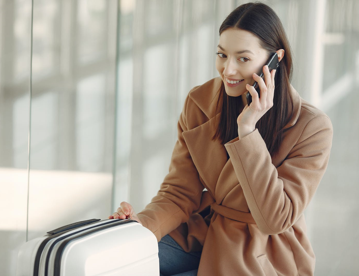 Dark haired woman in a tan coloured coat, talking on the phone