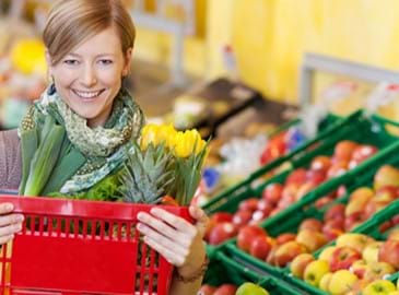 A smiling woman holding a red shopping basket in a grocery store 
