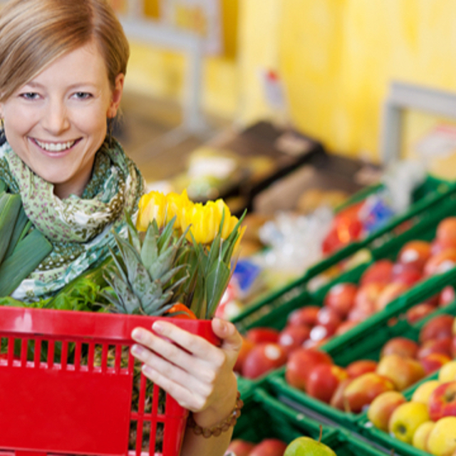 A smiling woman holding a red shopping basket in a grocery store 
