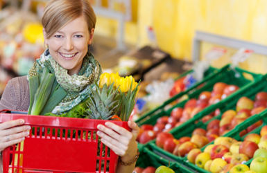 A smiling woman holding a red shopping basket in a grocery store